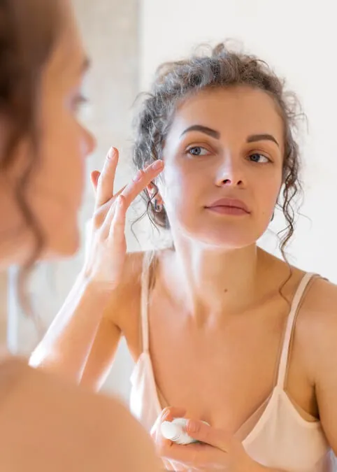 woman looking mirror applying cream face 1