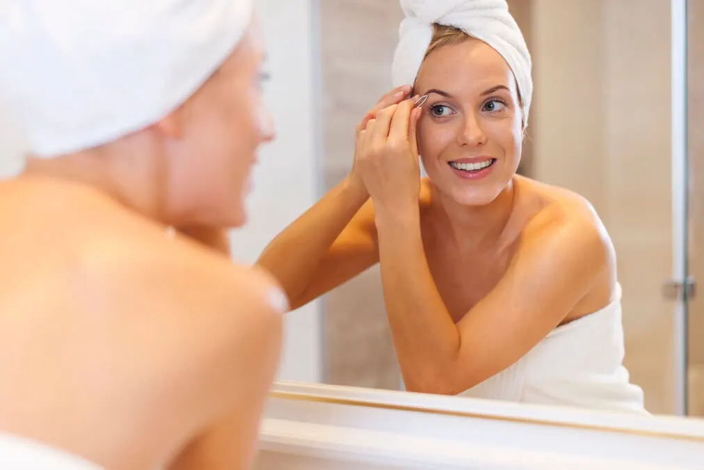 woman tweezing eyebrows front mirror 1